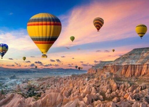 Gambar panorama lembah Cappadocia saat matahari terbit, menampilkan kerucut batu yang ikonik dan balon udara yang melayang di langit yang berwarna-warni, menciptakan pemandangan yang memukau dan unik
