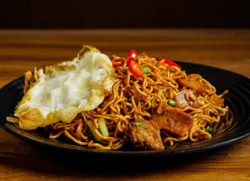 Sepiring mie goreng pedas dengan taburan cabai merah dan topping ayam suwir